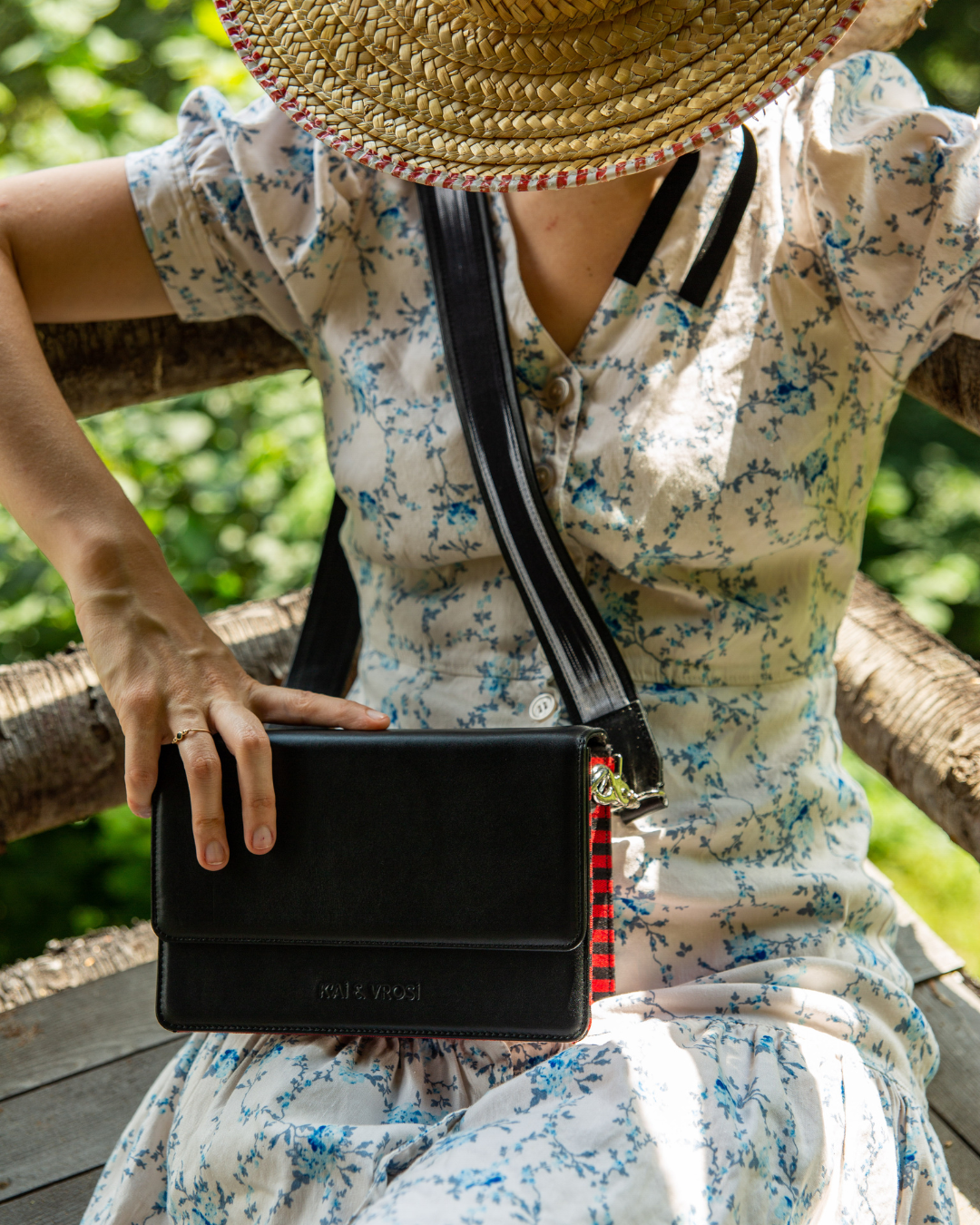 A woman wearing dress with floral pattern wears Loya black leather crossbody bag